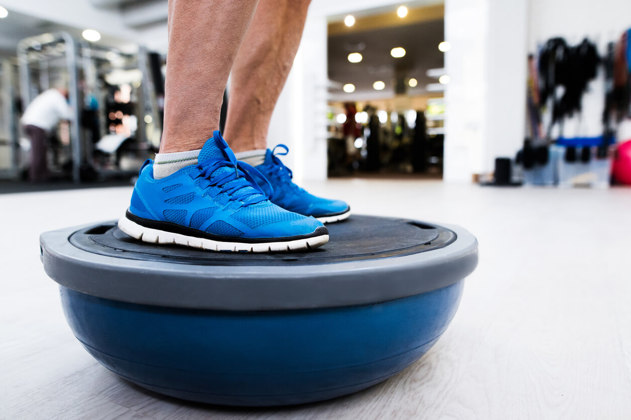 Close up of legs of senior man in gym standing on bosu balance ball and exercising as part of bodybuilding training